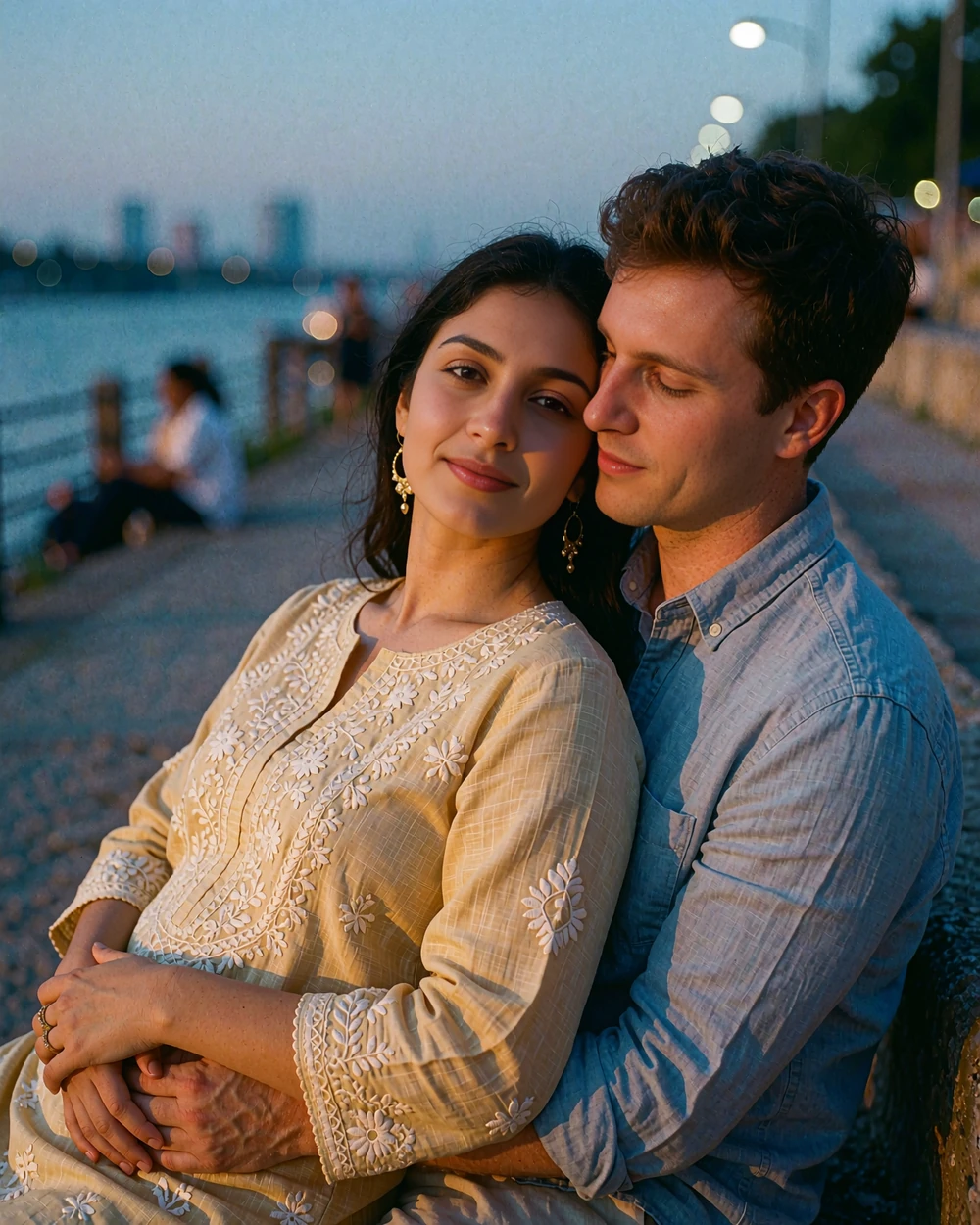 Pakistani woman in a beige embroidered kurta standing with a Western man on a riverside promenade at dusk