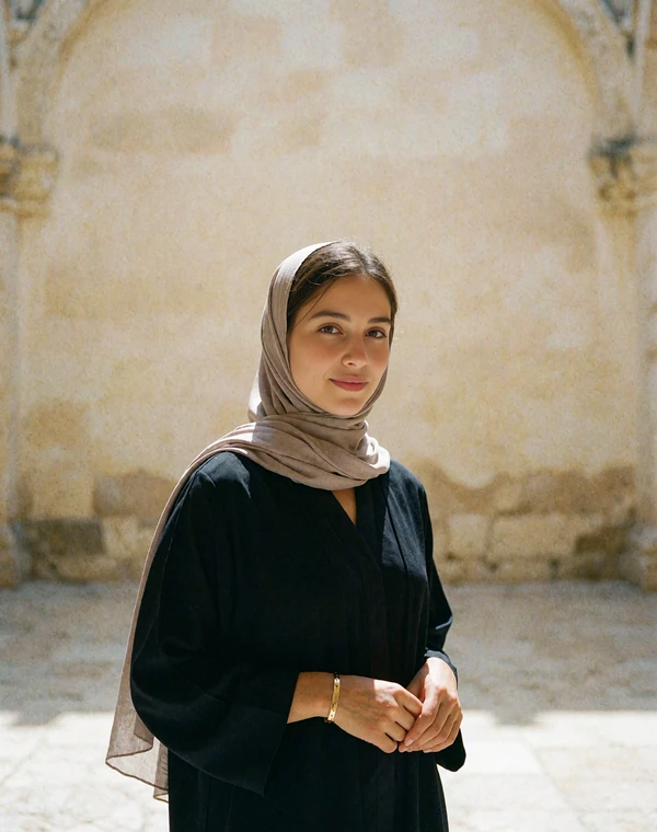 Yemeni woman in a dove-grey headscarf and black abaya smiling in a sunlit stone courtyard